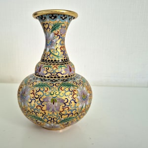 May include: A decorative, ornate vase with a bulbous body and a flared neck. The vase features a gold background with intricate floral patterns in blue, green, purple, and red. The rim is trimmed with gold.