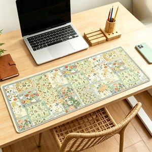 May include: A floral patterned desk mat with a light green and cream color scheme. The rectangular mat features a patchwork design with various flower and leaf patterns. A laptop, phone, and desk accessories are on the wooden desk.