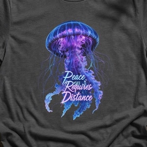 以下が含まれることがあります： 青と紫のクラゲのイラストが描かれた濃い灰色のTシャツ。「Peace Requires Distance」の文字がデザインに含まれています。クルーネックと半袖です。