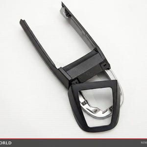 May include: Black plastic car interior trim piece with a silver-colored accent. The trim has a rectangular shape with a curved opening and two long, narrow extensions. The image is taken on a white background.