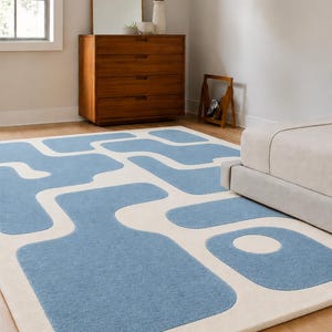 May include: A rectangular area rug featuring a cream-colored base with a repeating pattern of soft blue, rounded, abstract shapes. The rug has a textured pile surface and includes the text "MAHWAOR CARPETS" printed in the bottom left corner.