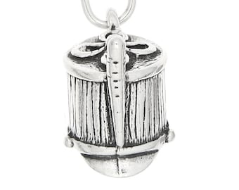 May include: A silver charm in the shape of a small drum with a decorative design. The drum has a textured surface and a small loop at the top for attaching to a bracelet or necklace.