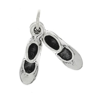 May include: A silver charm featuring a pair of ballet slippers. The charm is detailed with the shape of the shoes and the interior of the slippers. The charm is suspended from a small loop.
