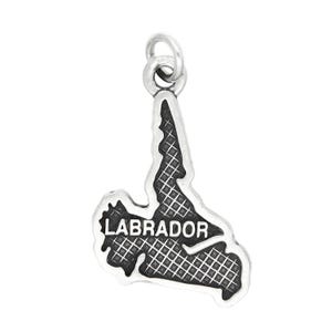 May include: A silver-colored charm in the shape of the Labrador region, with the word "LABRADOR" in capital letters. The charm has a textured, grid-like pattern within the outline.