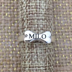 May include: Silver dog bone ring with the name "MILO" engraved on it.