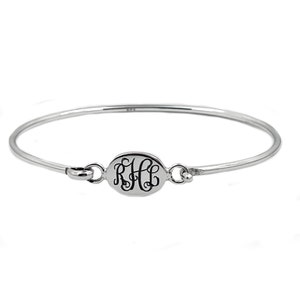 May include: A silver bangle bracelet with a round charm featuring a monogrammed inscription of "RHL".