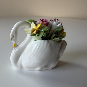 Może przedstawiać: Zestaw trzech ceramicznych kubków z nakrapianym, matowym wykończeniem. Kubki są w odcieniach kremu, jasnoszarym i ciemnoszarym. Każdy kubek ma prosty, nowoczesny design i zaokrąglony uchwyt.