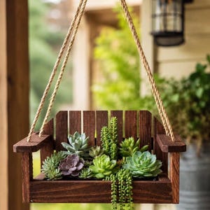 May include: A hanging planter shaped like a miniature wooden Adirondack chair, featuring a dark brown stained finish and thick jute rope for suspension. The seat is filled with a variety of green and purple succulents, including trailing vines.