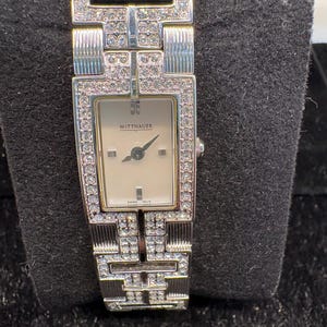 May include: A silver-tone Wittnauer wristwatch with a rectangular face and a light-colored dial. The bezel and the link bracelet are encrusted with clear crystals in a geometric pattern. The dial features black hands and the text Wittnauer.
