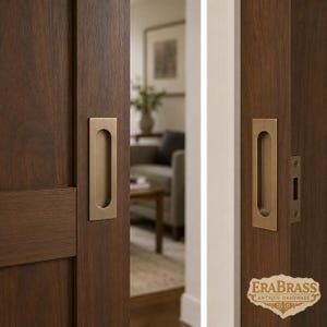 Peut inclure: Deux poignées encastrées rectangulaires en laiton installées sur des portes coulissantes en bois brun foncé. La quincaillerie présente une finition métallique mate lisse avec une zone de préhension encastrée. Une petite plaque est visible.