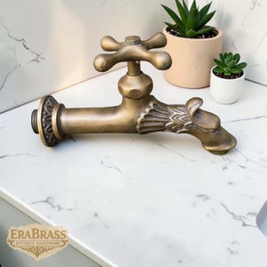 May include: Antique brass faucet with a cross-shaped handle and a decorative dragon head spout. The faucet is a warm gold color and features intricate detailing. The faucet is a vintage style and is suitable for a bathroom or kitchen.