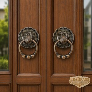 May include: Two bronze-toned metal door knockers with a circular ring and a floral-shaped backplate mounted on a dark brown wooden door. The backplate features a textured centre and petal-like edges. The text EraBrass Antique Hardware is visible.
