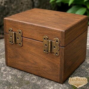 Op de afbeelding: Een rechthoekige houten doos met een donkerbruine afwerking en zichtbare houtnerf. Het deksel is aan de basis bevestigd met twee decoratieve antiek messing scharnieren met een geschulpte rand. De tekst EraBrass Antique Hardware is zichtbaar.