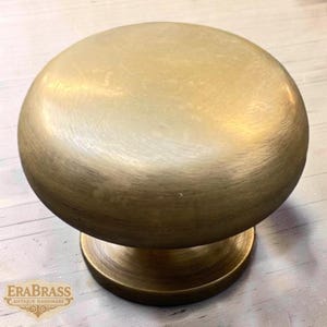 Puede incluir: Un pomo de armario de latón con una parte superior redonda en forma de cúpula y una base circular. El pomo tiene un acabado cepillado, lo que le da un aspecto vintage. El herraje es probablemente para muebles o armarios.