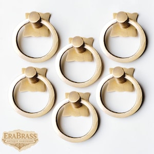 May include: Six antique brass ring pulls. Each pull features a circular ring attached to a decorative backplate with a central post. The pulls are arranged on a white background. The Era Brass logo is visible in the lower left corner.