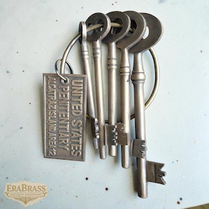 May include: A set of antique brass keys on a ring, with a rectangular tag that reads "UNITED STATES PENITENTIARY ALCATRAZ ISLAND AREA 2". The keys have intricate designs and are likely vintage.