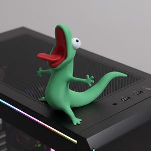 Op de afbeelding: Een groene hagedisachtige figuur met een rode mond en tong en een enkel wit oog. De figuur is geposeerd met uitgestrekte armen. Hij zit bovenop een zwarte computerkast.