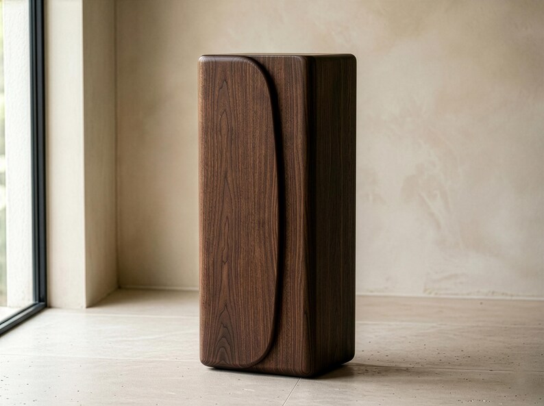 Op de afbeelding: Een hoge, rechthoekige houten kast met een donkerbruine afwerking. De kast heeft een gebogen designelement aan de voorkant. Het meubelstuk staat tegen een neutrale achtergrond en benadrukt de moderne, minimalistische esthetiek.