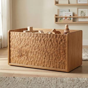 May include: A light brown wooden toy chest with a carved, textured front. The chest is filled with wooden toys, including blocks, a horse, and a stacking toy. The chest is rectangular with rounded corners.