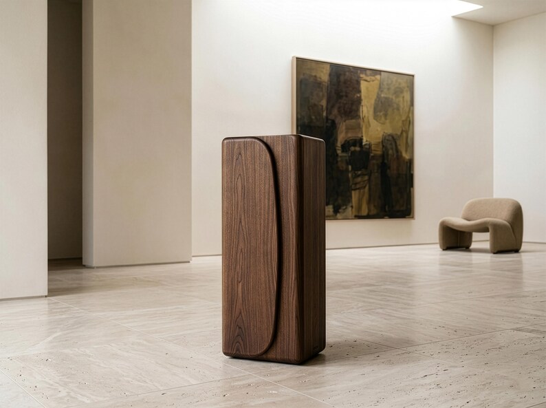 Op de afbeelding: Een hoge, rechthoekige houten kast met een gebogen ontwerp aan de voorkant. De kast is gemaakt van donkerbruin hout en staat op een lichtgekleurde tegelvloer. Op de achtergrond een schilderij en een beige stoel.