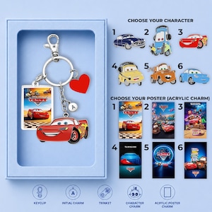 May include: A silver-toned metal keyring featuring a red car charm, a rectangular acrylic charm with a movie poster graphic, a small red heart charm, and a circular charm with the letter A. The keyring is displayed in a light blue box.