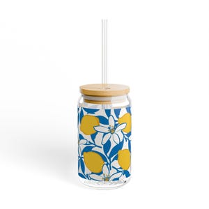 Peut inclure: Un verre transparent avec un couvercle en bambou et une paille transparente. La tasse présente un motif répété de citrons jaunes, de fleurs blanches et de feuilles bleues sur fond blanc. Conçu pour les boissons froides.