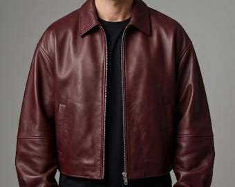 May include: A deep burgundy leather jacket featuring a classic collar, long sleeves with cuffs, and a full-length front zipper closure. The jacket is worn over a plain black t-shirt, showcasing a smooth, matte finish and a structured, waist-length fit.