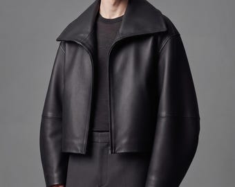 May include: A black leather jacket featuring a wide, oversized collar and a front zipper closure. The jacket has long, loose sleeves and a cropped hemline, worn over a dark charcoal crew neck shirt and matching dark charcoal trousers.