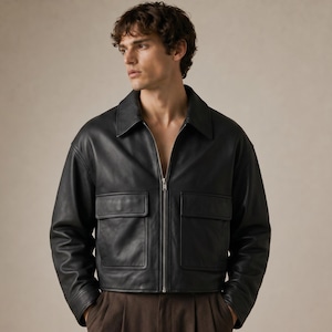 May include: A black leather jacket with a collared neckline and a silver zipper closure. The jacket features two square pockets on the front and long sleeves. The jacket is a cropped style.