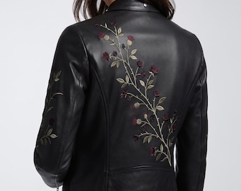 May include: A black leather jacket featuring an intricate embroidered design of climbing rose vines with dark red flowers and sage green leaves. The embroidery extends across the back panel and down the sleeves, showcasing detailed stems and thorns.