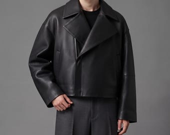 May include: A black leather jacket with a wide notched collar, long sleeves, and a cropped silhouette. The jacket features a double-breasted front closure with a smooth finish, clean lines, and a structured fit that sits at the waistline.