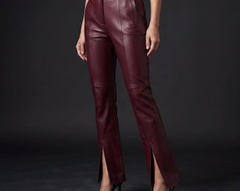 May include: High-waisted trousers in a deep burgundy leather finish. These pants feature a structured waistband, vertical seam detailing down the front of each leg, and a distinct vertical slit at the bottom hem of each pant leg, ending above the ankle.