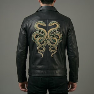 May include: A black leather jacket featuring a large, symmetrical embroidery on the back. The design depicts two intertwined snakes in shades of gold and dark green, with detailed scales and coiled bodies centred across the shoulder blades.