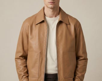 May include: A tan leather jacket with a collared neckline and a front zipper closure. The jacket has two front pockets and long sleeves. The model is wearing a white t-shirt underneath the jacket.
