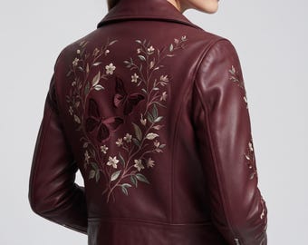 May include: A deep burgundy leather jacket featuring intricate embroidery on the back and sleeves. The design showcases delicate floral branches and two prominent butterflies in shades of dark red, pink, and muted green, with a classic collar.