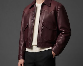 May include: A deep burgundy leather jacket featuring a pointed collar, a front zipper closure, and two large flap pockets on the chest. The jacket is worn over a cream-colored knit sweater and paired with black trousers, creating a layered look.
