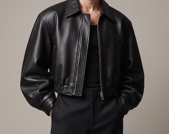 May include: A black leather jacket with a classic collar, long sleeves, and a front zipper closure. The jacket features a cropped length with an elasticized hem, worn over a black tank top and paired with black trousers.