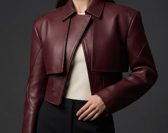 May include: A cropped burgundy jacket with a smooth finish, featuring a structured collar, long sleeves, and a layered front panel design. The jacket is worn over a plain white top and black trousers, showcasing a clean, tailored silhouette.