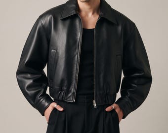 May include: A black leather jacket with a classic collar, long sleeves, and a front zipper closure. The jacket features a cropped length with an elasticized hem, side pockets, and a smooth finish, worn over a black tank top and black trousers.