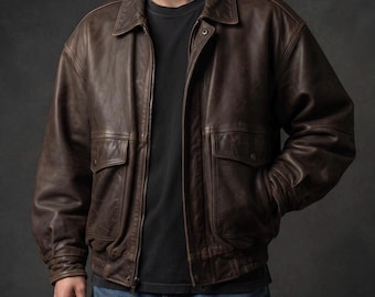 May include: A dark brown leather bomber jacket featuring a classic collar, a full-length front zipper, and two large flap pockets on the front. The jacket has ribbed cuffs and a ribbed hem, worn over a plain black t-shirt and blue denim jeans.