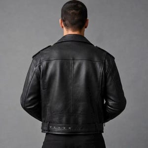 May include: A black leather motorcycle jacket featuring a classic fold-down collar, shoulder epaulets, and a horizontal back yoke. The jacket includes a buckled belt at the waist with metal eyelets and long sleeves, shown from the back view.