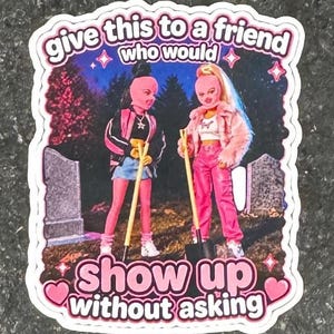 May include: A sticker with a pink and white border featuring two doll figures with shovels in a graveyard scene. The sticker has the text "give this to a friend who would" and "show up without asking."