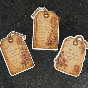 May include: Three vintage-style gift tags with romantic quotes and floral accents. Each tag features a distressed paper design, postage stamps, and a twine loop for hanging. The tags have quotes like "Forever wasn't long enough with you."
