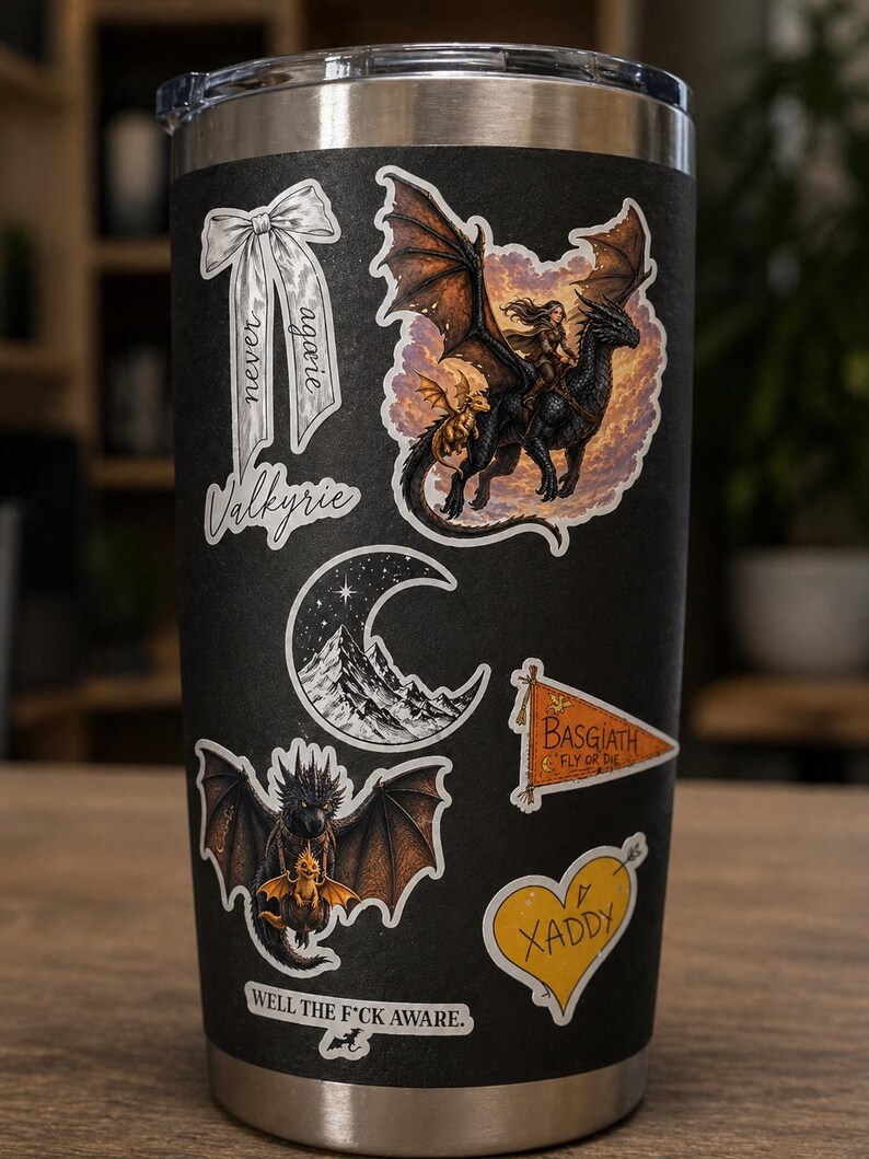 May include: Black tumbler covered in fantasy-themed stickers. Stickers include a dragon rider, a dragon with a smaller dragon, a mountain scene, a banner that says "BASGIATH FLY OR DIE", a heart that says "XADDY", and a bow that says "never again Valkyrie".