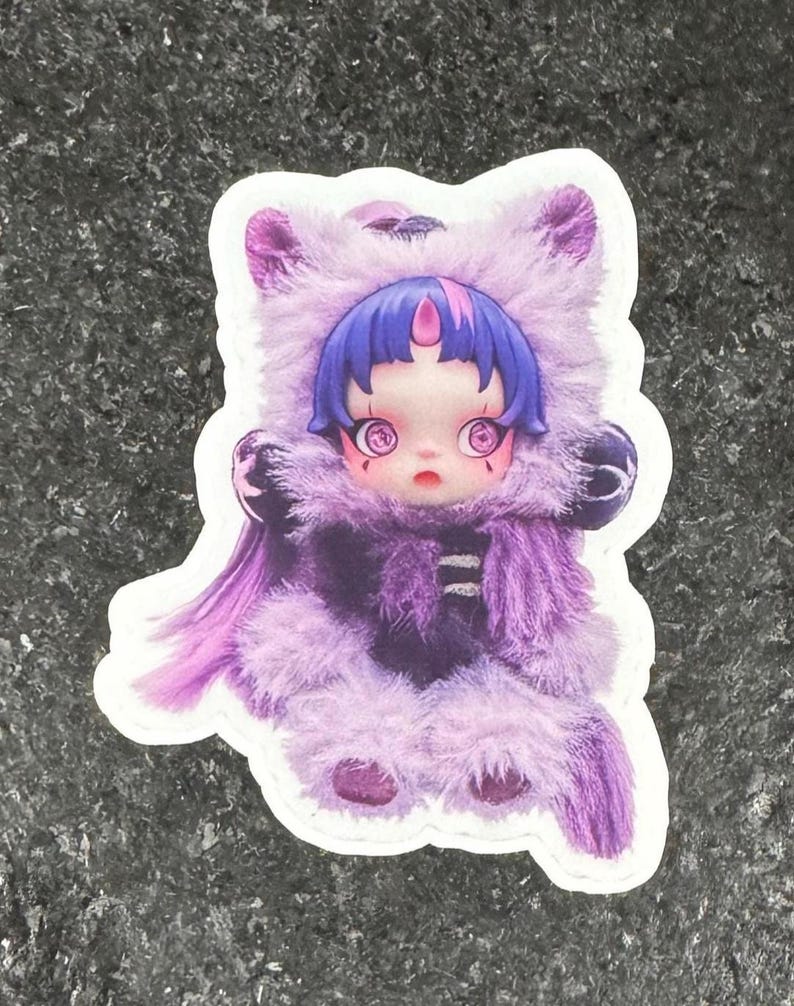 K&ouml;nnte beinhalten: Ein Aufkleber mit einer stilisierten Illustration einer puppenartigen Figur in einem lila Fellkost&uuml;m. Die Figur hat blaue Haare, gro&szlig;e Augen und einen kleinen Mund. Das Kost&uuml;m hat eine Kapuze und einen Knopfverschluss.