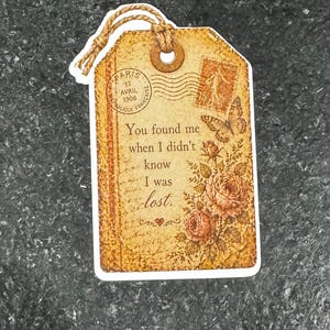 May include: A vintage-style gift tag with a distressed, sepia-toned design. The tag features floral and butterfly illustrations, along with the text "You found me when I didn't know I was lost." A twine loop is attached.