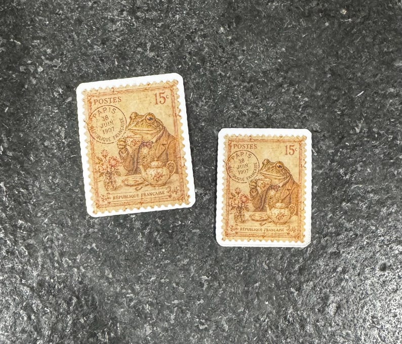Op de afbeelding: Twee vintage postzegels. Elke postzegel toont een kikker in een pak die thee drinkt, met de tekst "Postes" en "R&eacute;publique Fran&ccedil;aise". De postzegels zijn bruin met witte randen.