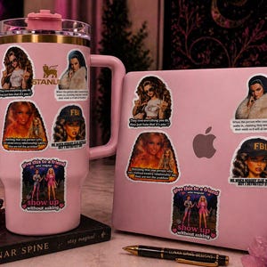 May include: A pink Stanley tumbler and a pink laptop are adorned with stickers featuring images of women and text. The stickers include phrases like "They love everything you do, they just hate that it's you." and "Give this to a friend, show up without asking."