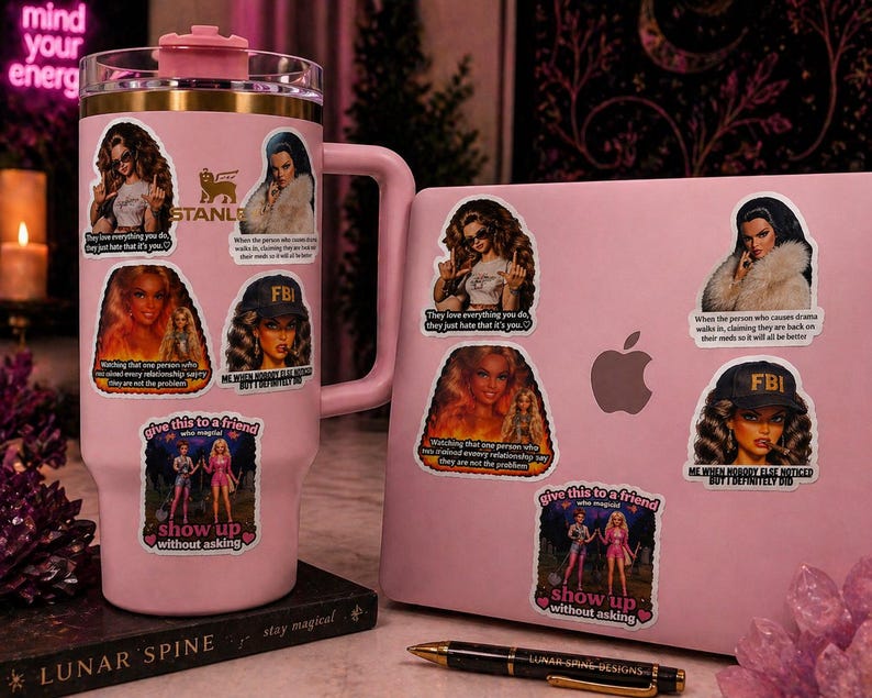 May include: A pink Stanley tumbler and a pink laptop are adorned with stickers featuring images of women and text. The stickers include phrases like "They love everything you do, they just hate that it's you." and "Give this to a friend, show up without asking."