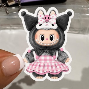K&ouml;nnte beinhalten: Ein Aufkleber mit einer Cartoonfigur in einem grauen, pelzigen Kost&uuml;m mit gro&szlig;en Ohren und einer rosa-wei&szlig;en Schleife. Die Figur tr&auml;gt ein rosa-wei&szlig; kariertes Kleid. Der Aufkleber hat einen wei&szlig;en Rand.
